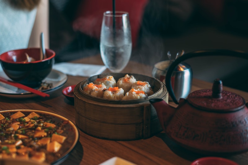 A table featuring dimsum, a Chinese tofu dish, a Chinese teapot and various tableware.